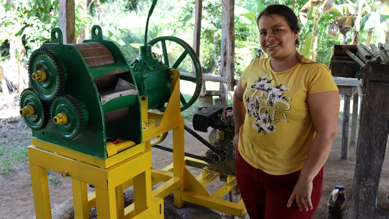 Une femme pose à côté d'un moulin à canne à sucre.