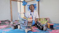 Vanessa Mwangani, kinésithérapeute spécialisée dans la thérapie de stimulation pour enfants. Elle travaille pour HI dans la province du Nord Kivu, en RDC. Portrait de Vanessa assise dans une salle. Elle tient un ballon dans les mains et autour d'elles sont disposés des jeux d'éveil pour enfants.