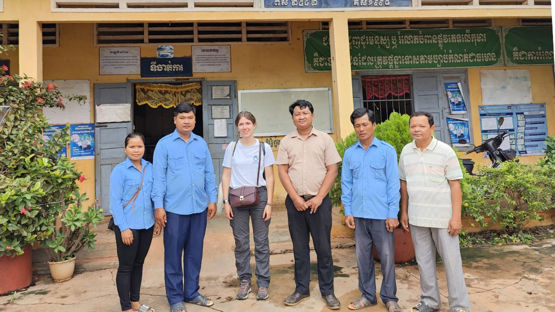 Un groupe de personnes debout devant un bâtiment avec des inscription en langue cambodgienne